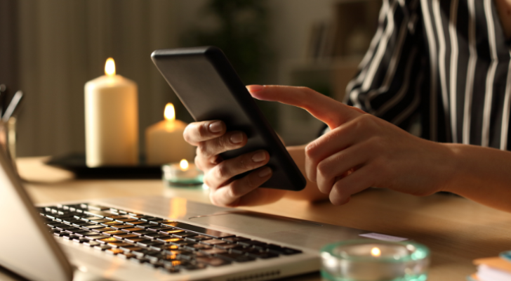 صورة تعبيرية لفتاة تحمل جهازها الخلوي وبجواراها شمعة