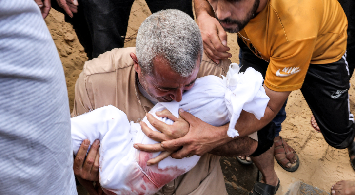 فلسطيني يحمل طفلا استشهد في قصف الاحتلال الإسرائيلي على قطاع غزة