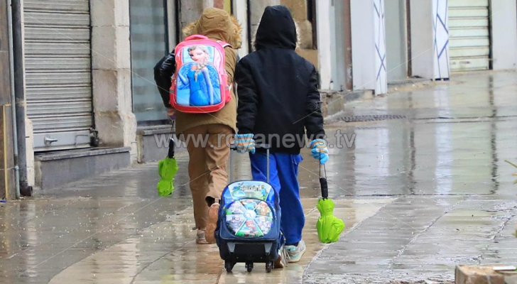 طلبة مدارس يمشون تحت المطر في عمان