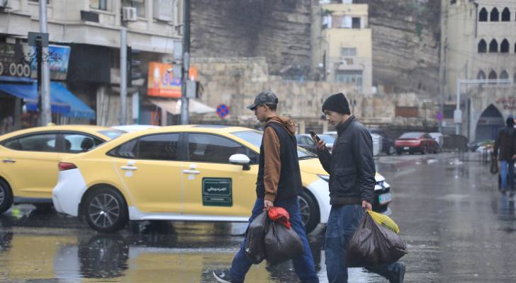 رجلان يسيران تحت المطر في العاصمة عمان