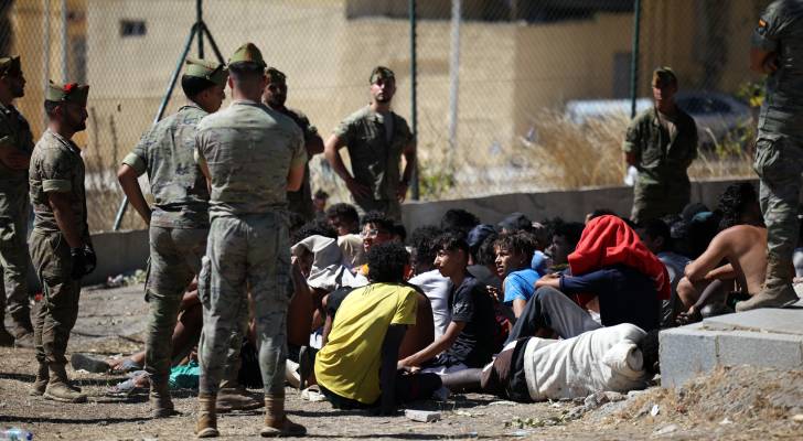 جنود مشاة إسبان يراقبون مجموعة من المهاجرين يجلسون على الأرض في جيب سبتة الإسباني